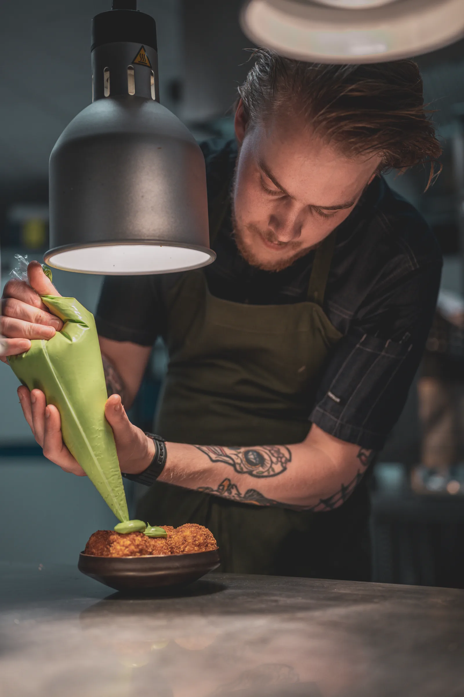 A chef finishing a dish under the pass lights